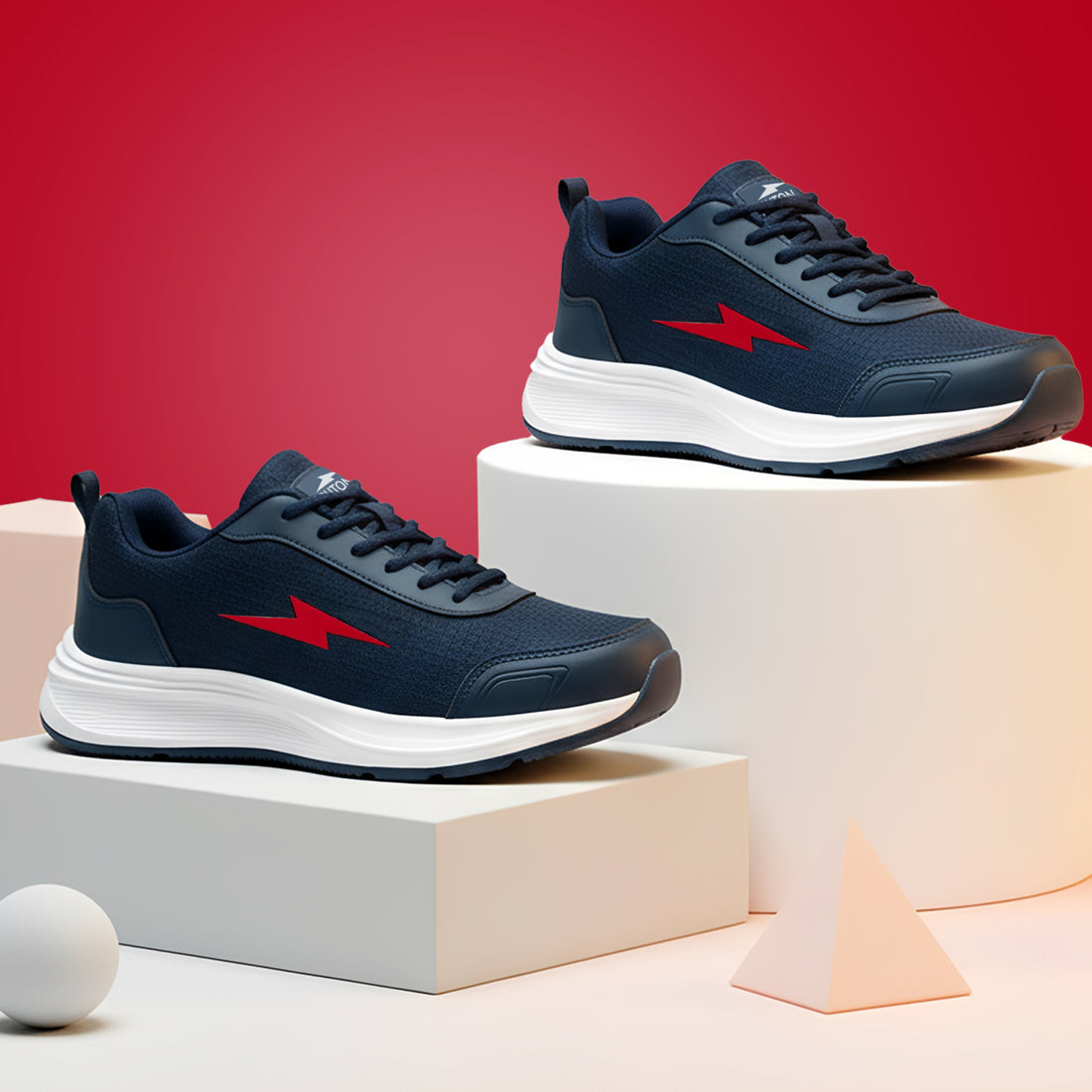 A pair of navy blue athletic sneakers with red lightning-bolt logos and white soles, displayed on white pedestals against a red background.